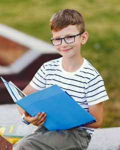 Pupil spend time in a school yard Pupil near school. Boy sitting with a folder.